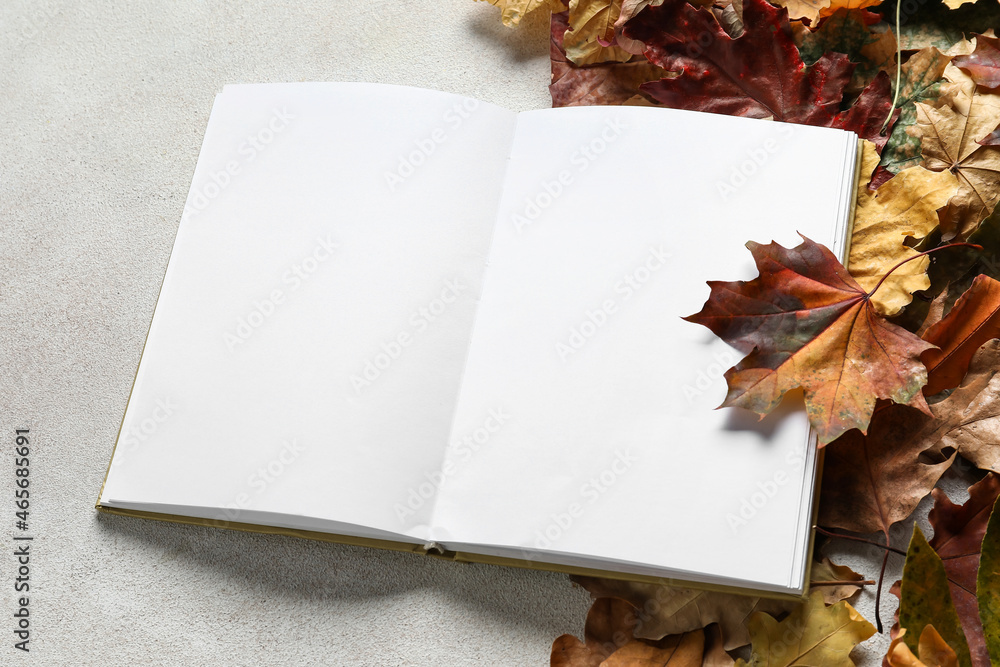 Blank open book and autumn leaves on light background