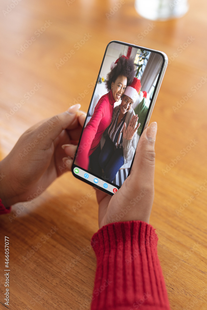 Hands holding smartphone with happy mother and daughter in christmas santa hat on video call screen