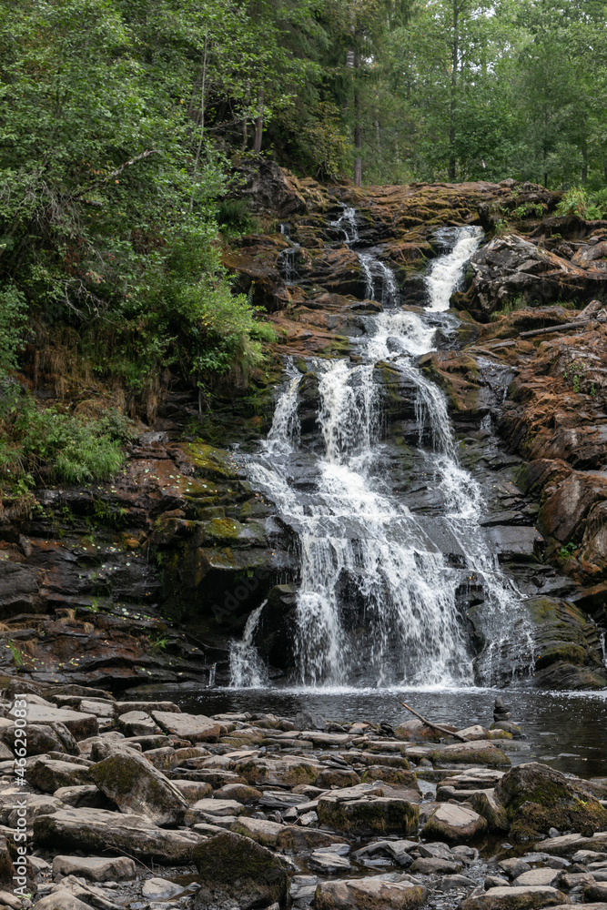 一个高高的瀑布，位于绿色的北方森林中央。瀑布周围的岩石崎岖不平