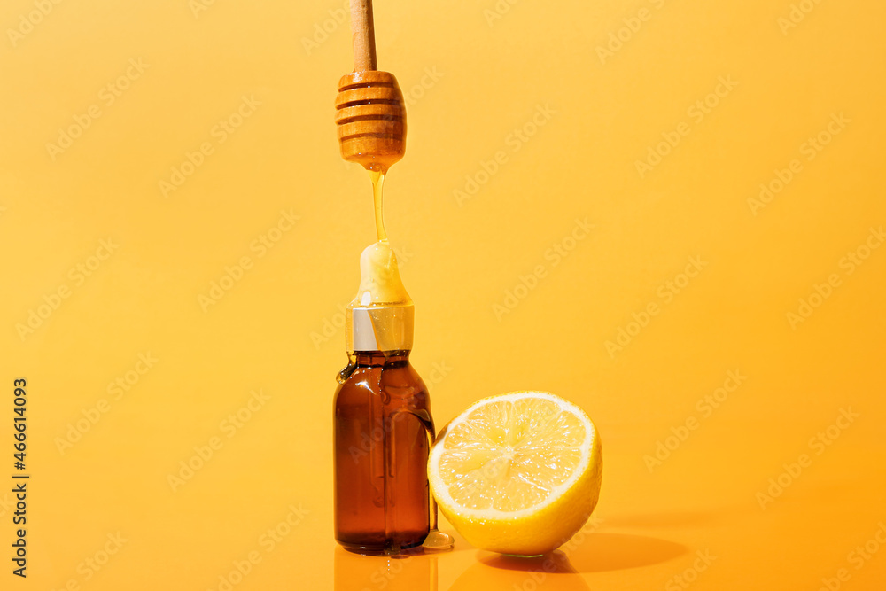 用勺子将蜂蜜倒在彩色背景的精油瓶上，特写