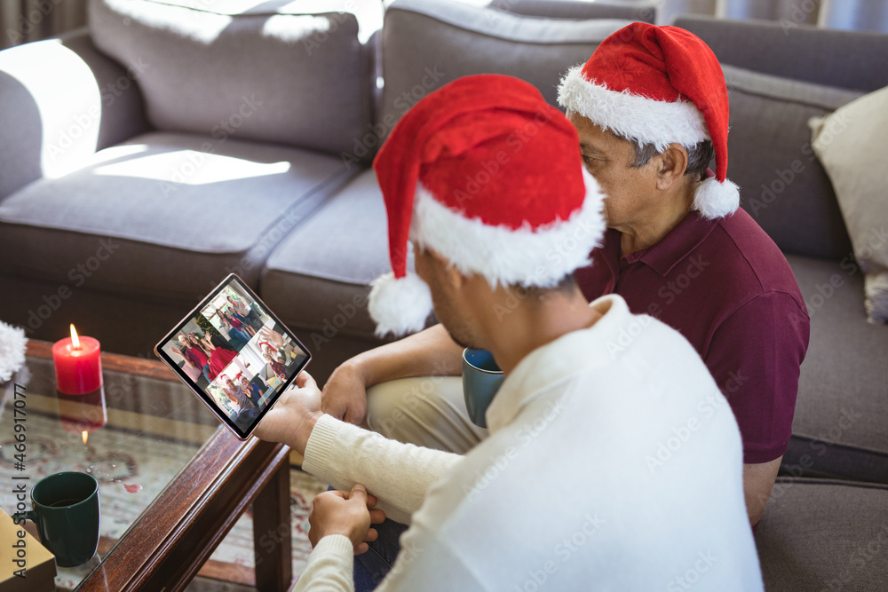 戴着圣诞老人帽的混血父亲和成年儿子与朋友进行平板电脑圣诞群视频通话