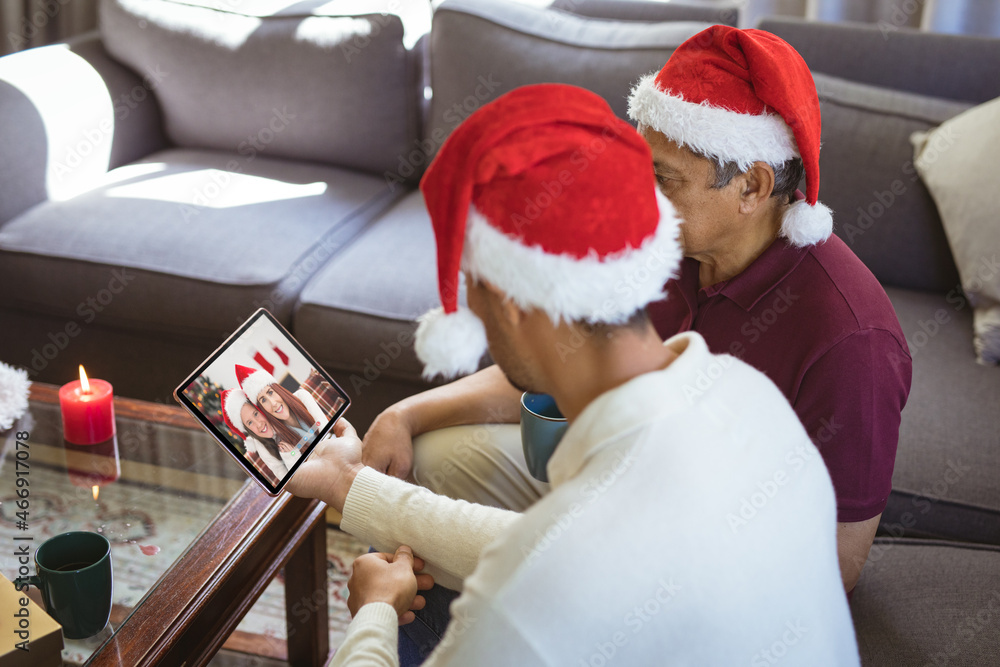 戴着圣诞老人帽的混血父亲和成年儿子与朋友进行平板电脑圣诞视频通话