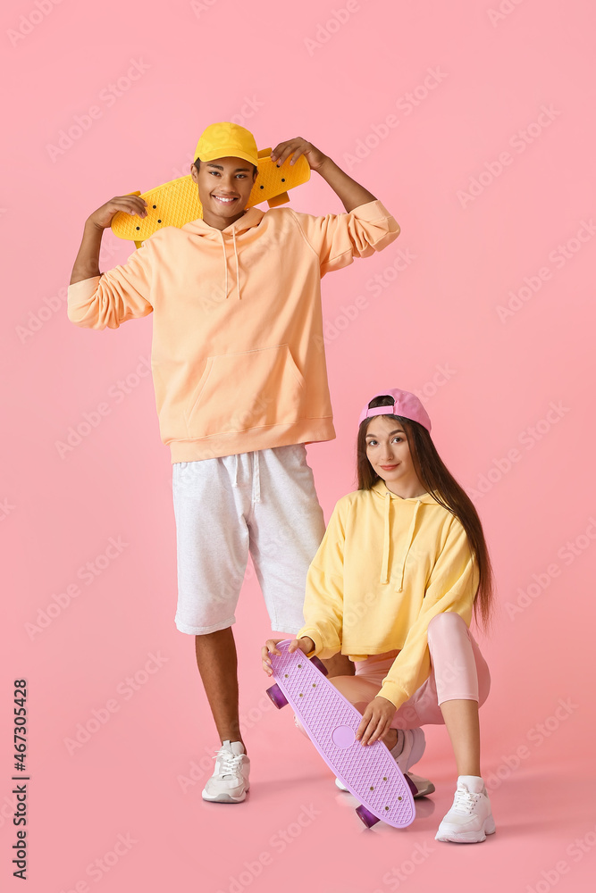 时尚的年轻滑冰情侣穿着粉色背景的连帽衫