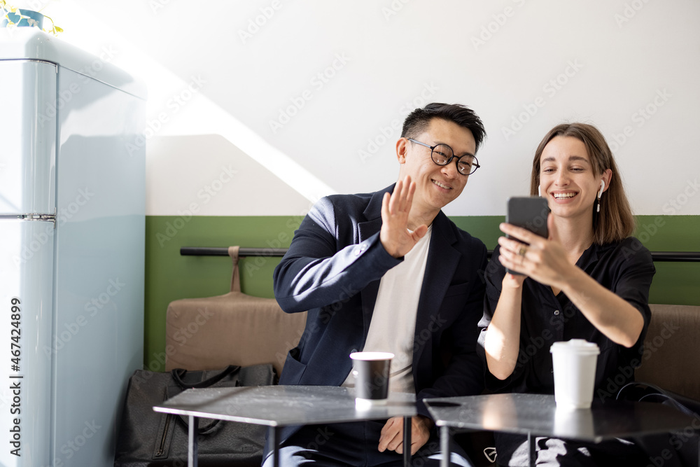 Smiling multiracial couple having video call on smartphone in cafe. Concept of rest and leisure. Ide