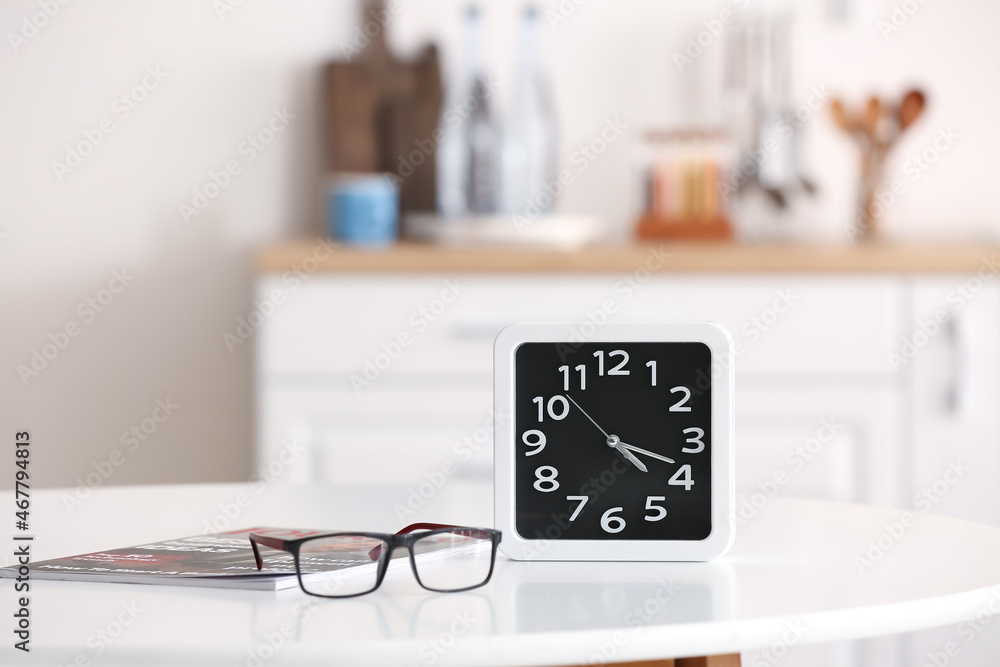 Clock with magazine and eyeglasses on table in kitchen