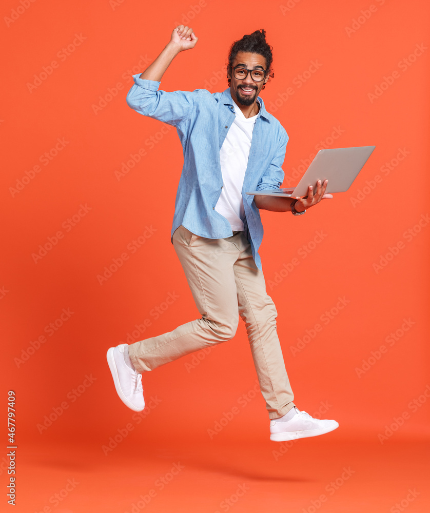 年轻、快乐、欣喜若狂的非裔美国人，笔记本电脑在橙色背景上跳跃