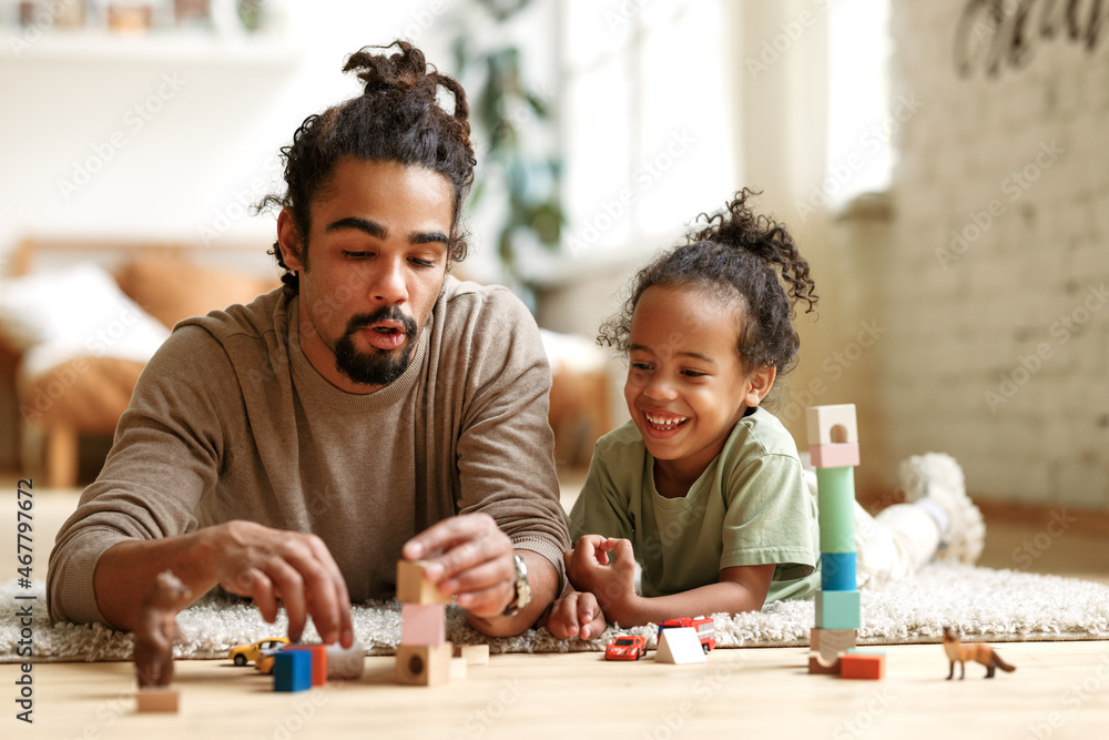 Happy african american family father and child son laughing while playing toys together at home