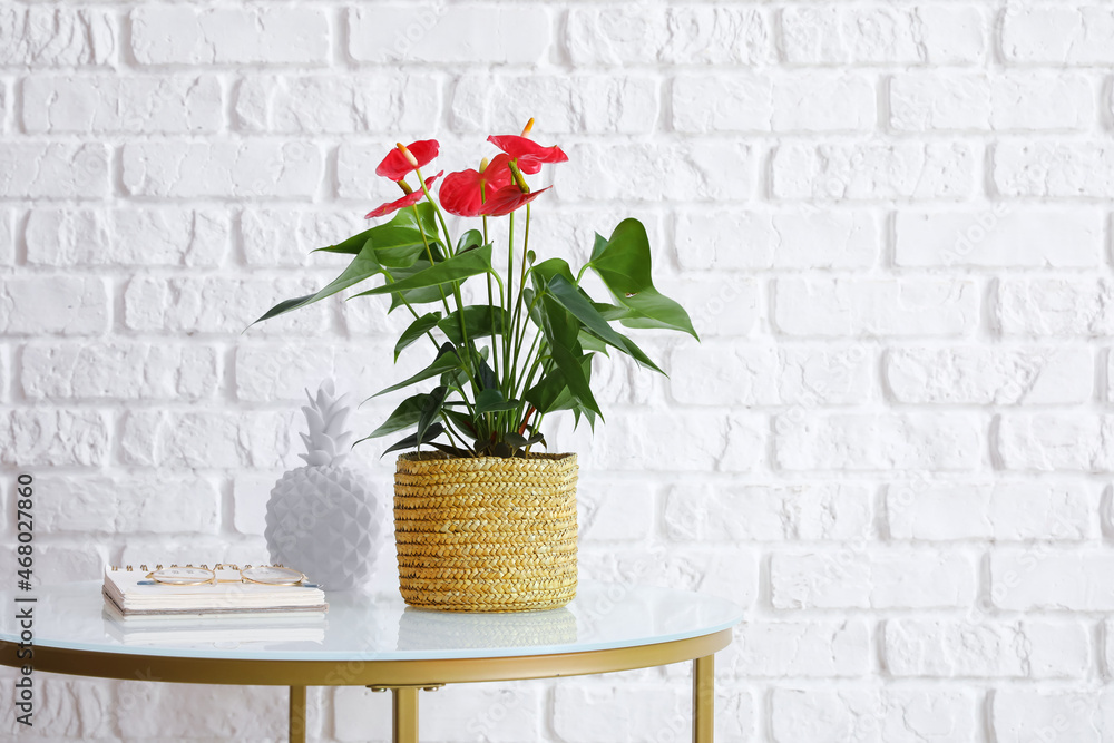 Table with Anthurium flower, notebook and eyeglasses on white brick background