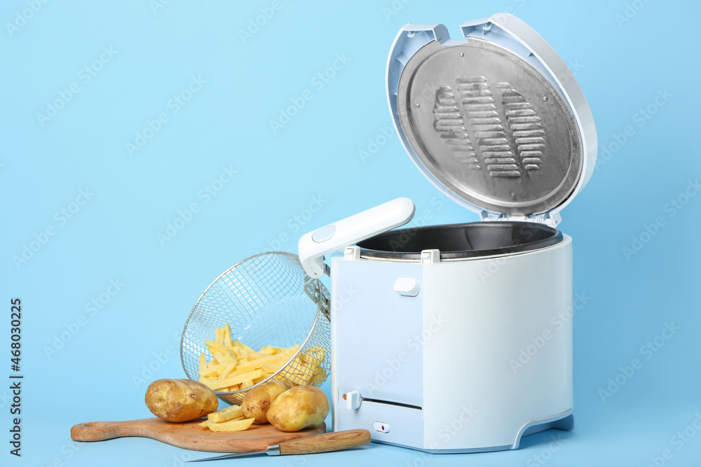 Modern deep fryer with potatoes on color background
