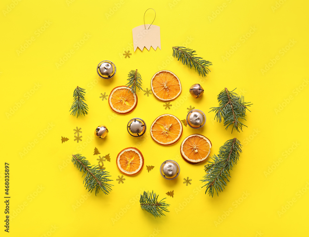 黄色背景下由冷杉树枝、铃铛和橙子制成的圣诞球
