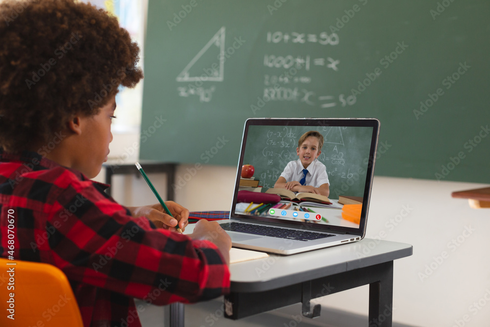 非裔美国男孩使用笔记本电脑进行视频通话，屏幕上是白人小学生