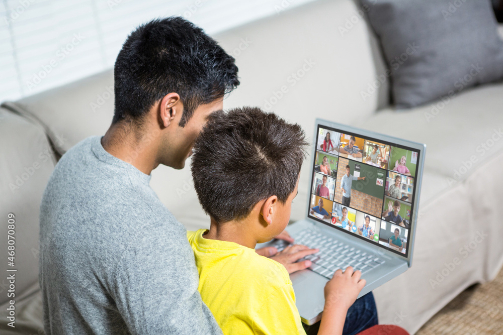 Biracial boy with father using laptop for video call, with elementary school pupils on screen