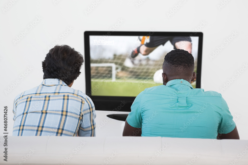两个朋友坐在家里一起看电视足球赛的后视图