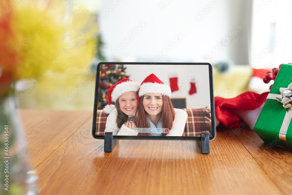 平板电脑上戴着圣诞老人帽微笑的高加索母女圣诞视频通话界面屏幕
