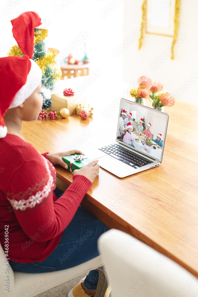 African american woman in santa hat making laptop christmas video call with smiling caucasian family