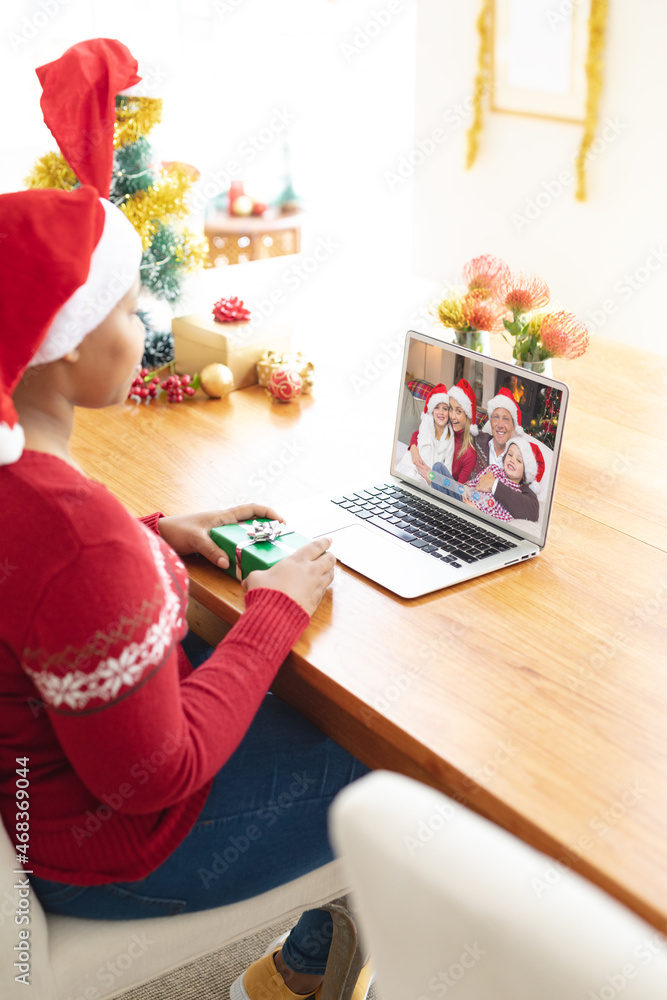 戴圣诞老人帽的非裔美国妇女与戴圣诞老人帽子的家人进行笔记本电脑圣诞视频通话