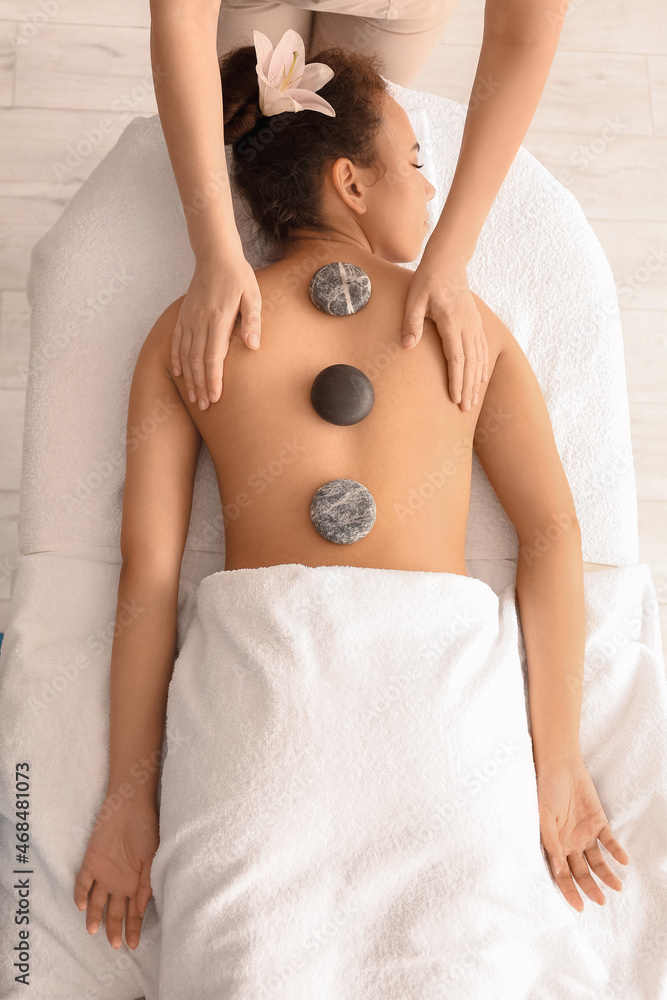 Young African-American woman getting massage with stones by therapist in spa salon