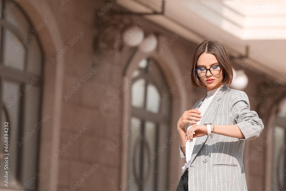时尚的女商人，带着时尚的配饰，在城市街道上查看时间