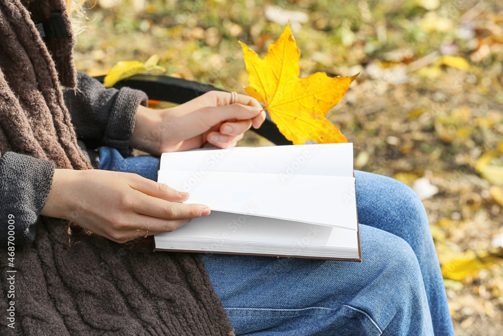 秋天公园里，女人拿着空白书页和树叶打开的书，特写