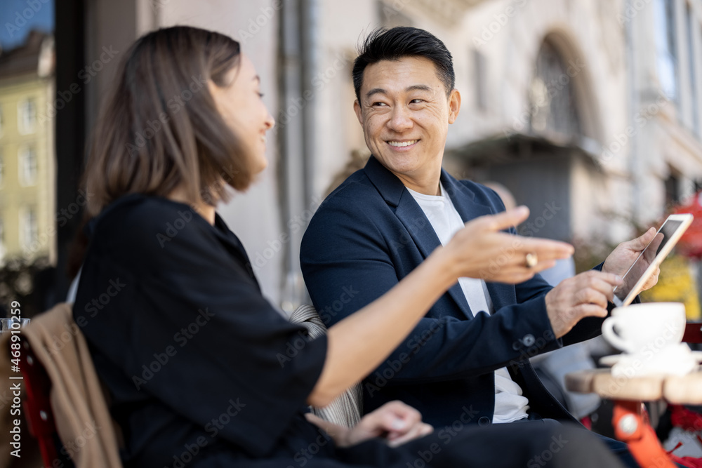 高加索女性和亚洲男性坐在户外咖啡馆进行商务对话。概念