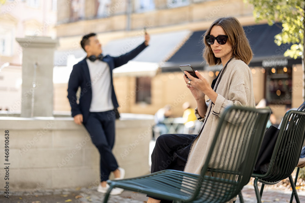 年轻女性和亚洲男性在带喷泉的城市区域使用智能手机。城市生活的概念。Beauti