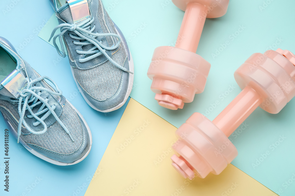 Dumbbells and shoes on color background