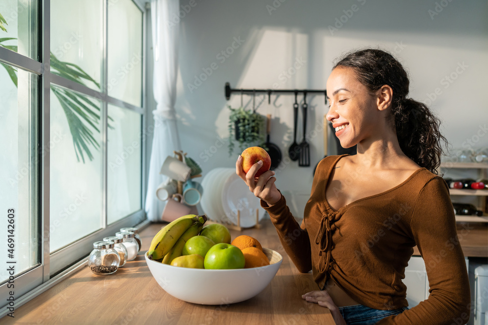 年轻漂亮的拉丁裔女性在家里厨房的桌子上吃水果。