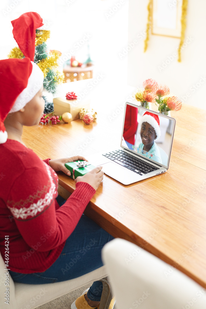 戴圣诞帽的非裔美国妇女与戴圣诞帽微笑的男孩进行笔记本电脑圣诞视频通话
