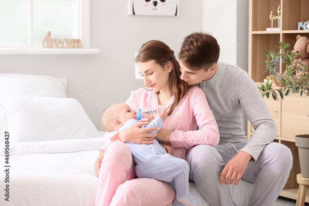 Young parents feeding little baby boy with bottle in bedroom