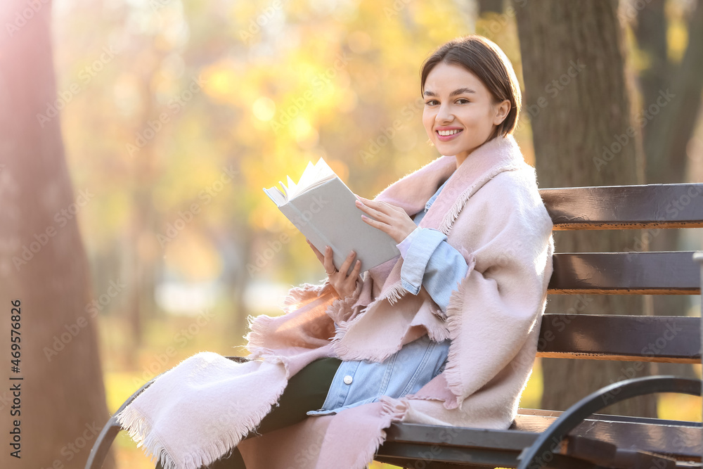 秋天公园里坐在木凳上，面带微笑的女人穿着格子布和书