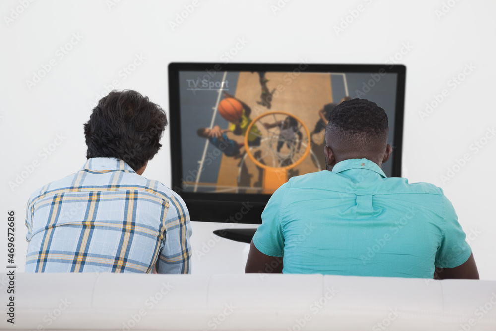 两个朋友坐在家里一起看电视上的篮球比赛的后视图