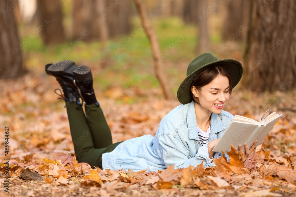 美丽微笑的女人躺在格子布上，在秋季公园看书