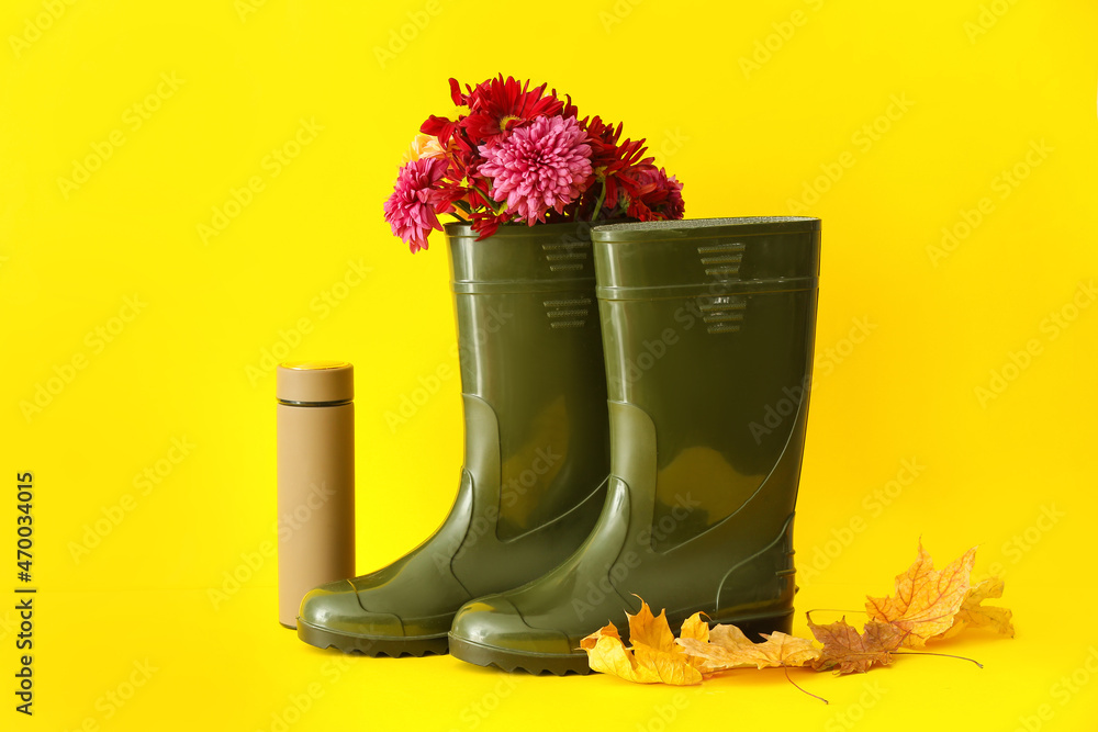 黄色背景上有花、保温瓶和落叶的橡胶靴
