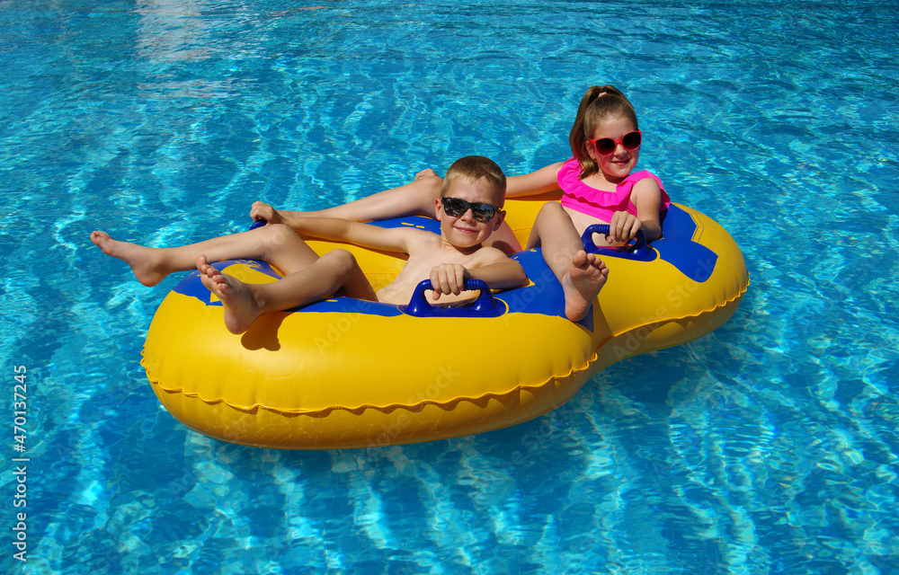 男孩和女孩在室外游泳池的充气浮子上。
