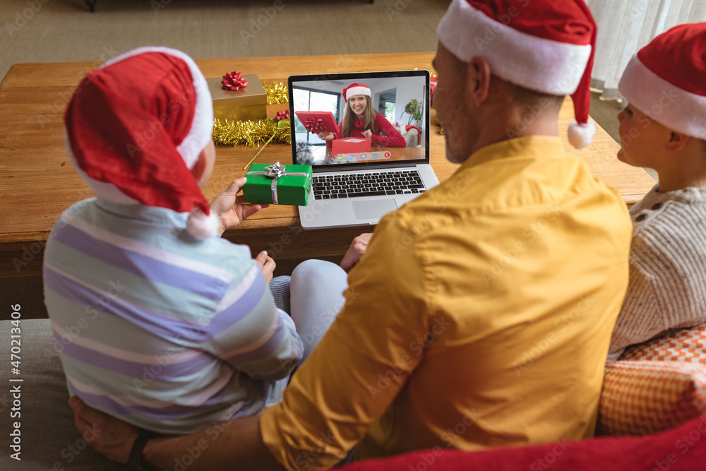 戴着圣诞老人帽的高加索父子与微笑的女人进行笔记本电脑圣诞视频通话