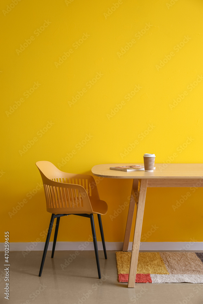 黄色墙壁附近的餐桌上放着纸杯咖啡和杂志