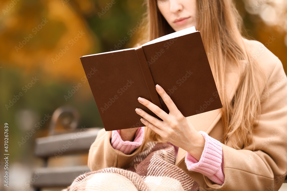 女子在秋季公园的长椅上读有趣的书，特写