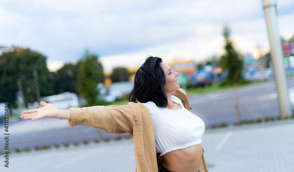快乐的高加索女性将手臂向两侧伸展。穿着米色外套的女性半转身站着
