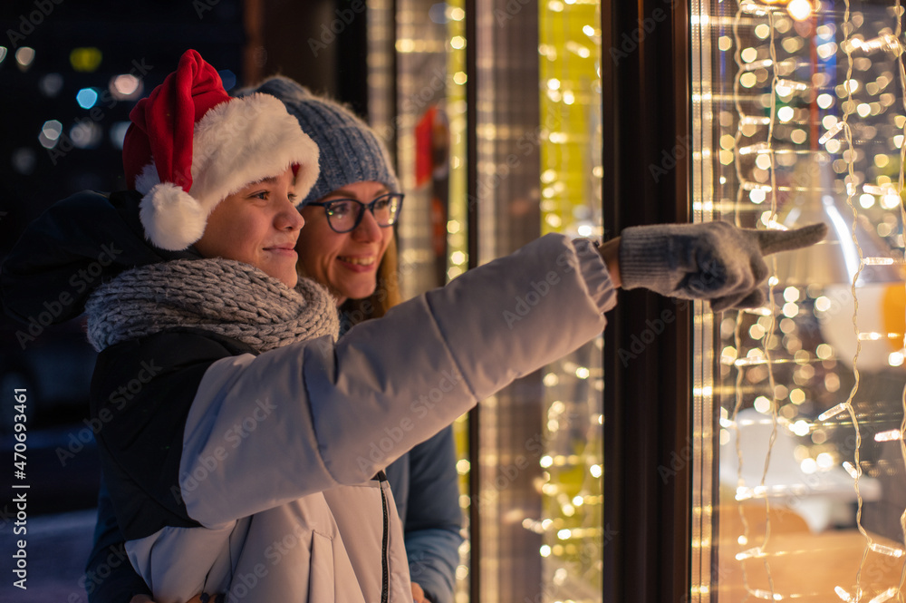 漂亮的女人和她儿子戴着圣诞帽，在明亮的商店橱窗里看着和做梦。圣诞礼物