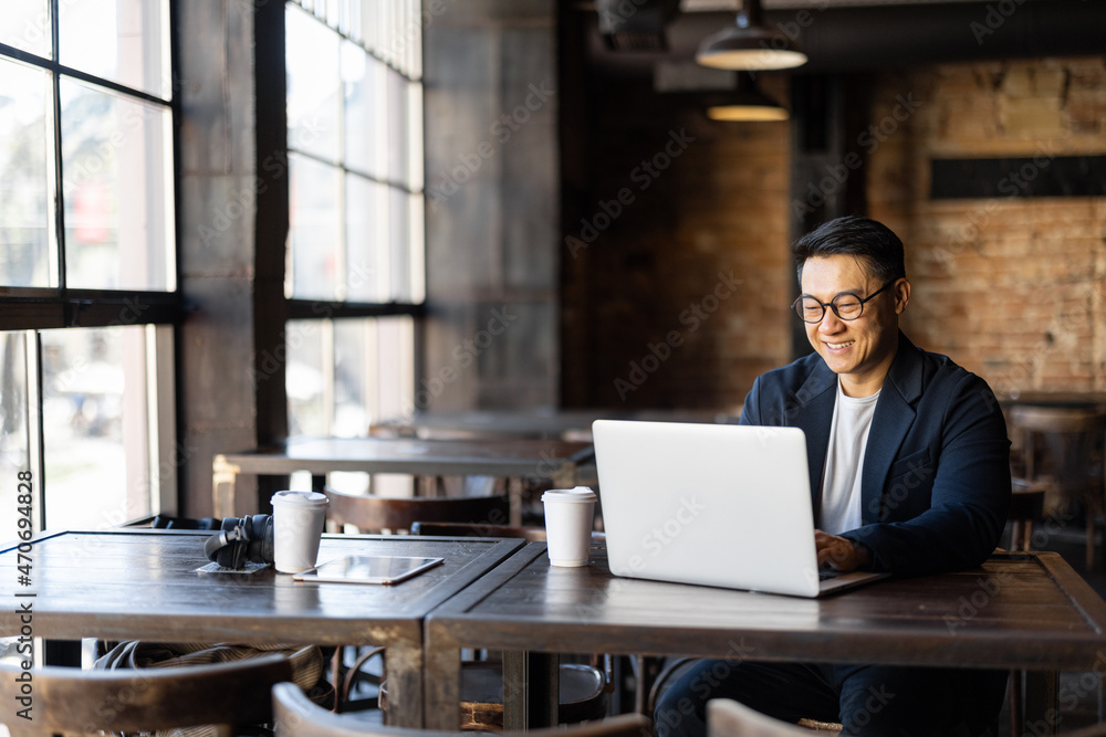 亚洲商人在咖啡馆工作时用笔记本电脑打字。远程和自由职业的概念。微笑