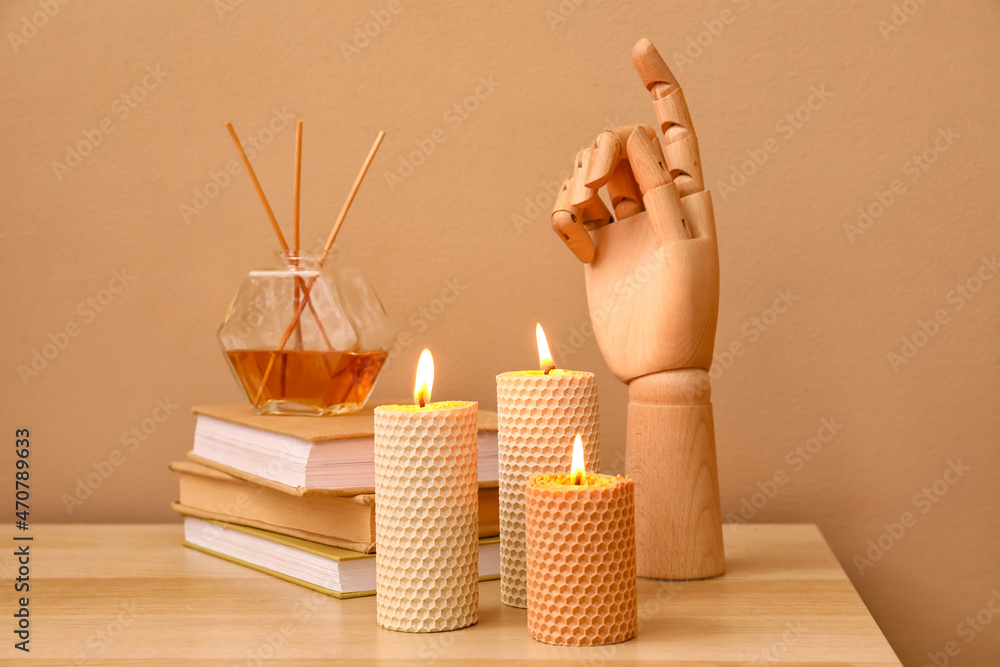 在彩色墙附近的木桌上燃烧蜡烛、木制手、一叠书和芦苇扩散器