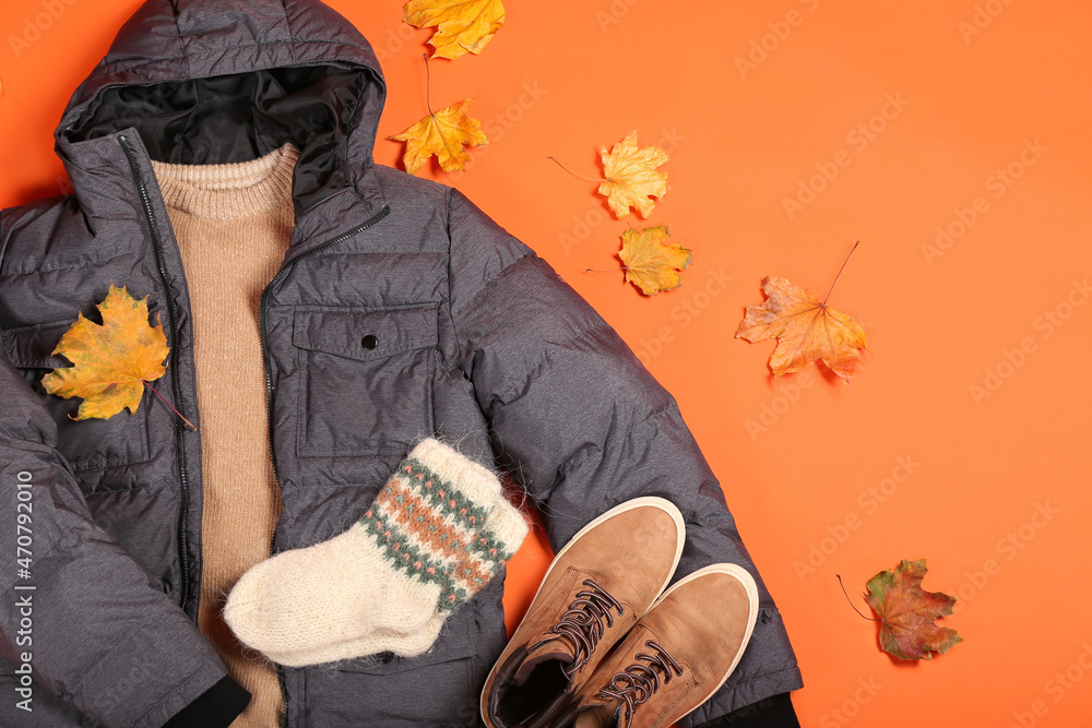 Stylish male jacket, sweater, socks, shoes and autumn leaves on color background