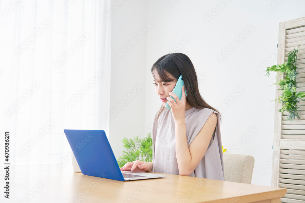 パソコンを見て電話する女性　リビング