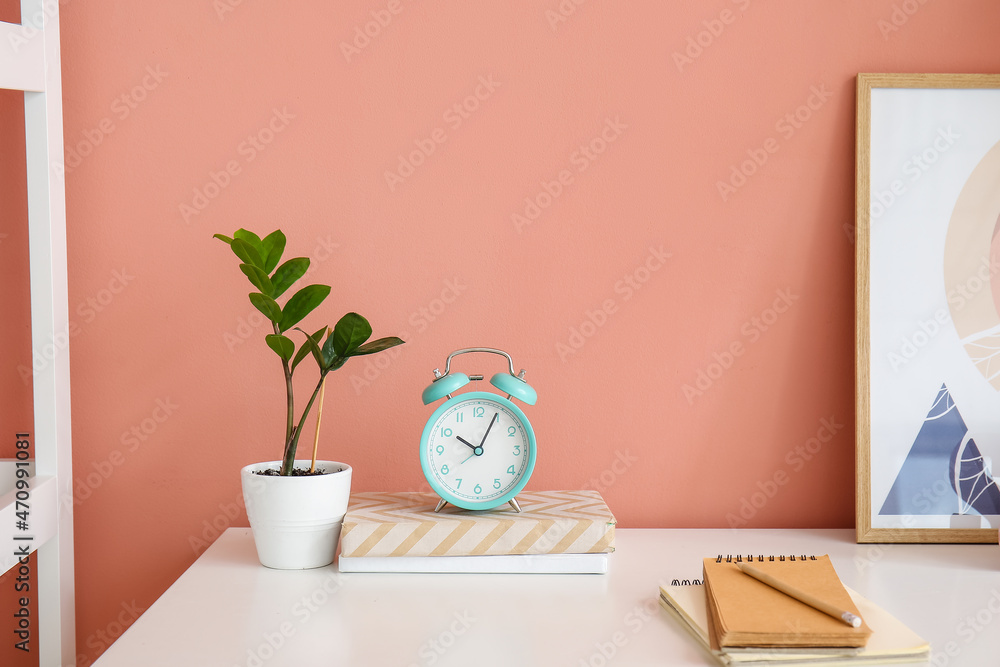 粉红色墙壁背景附近的桌子上有书籍、室内植物和装饰的闹钟