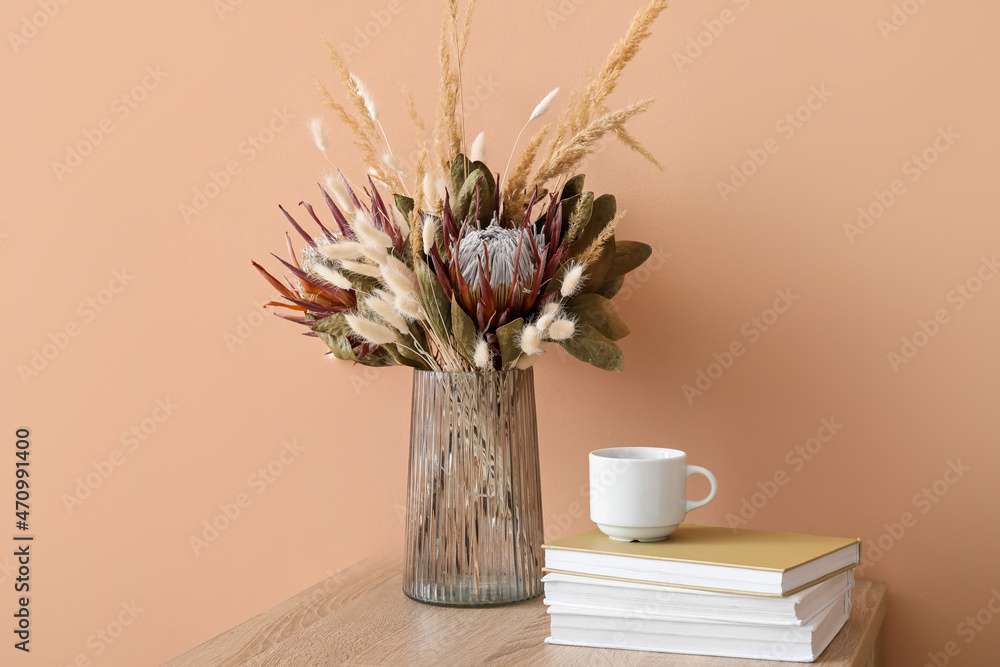 米色墙壁附近的桌子上放着一个花瓶，里面有漂亮的干花、书和杯子