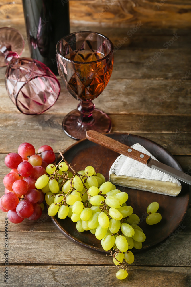 木制背景上有成熟的葡萄、奶酪和一杯葡萄酒的盘子