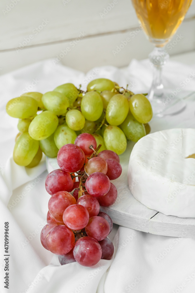 浅色背景上有成熟的葡萄、奶酪和一杯葡萄酒的木板
