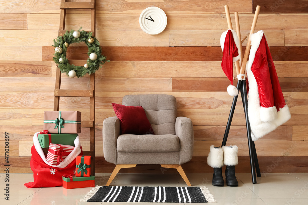 扶手椅上的枕头，装有圣诞礼物的袋子，木墙上挂着圣诞老人服装的衣架