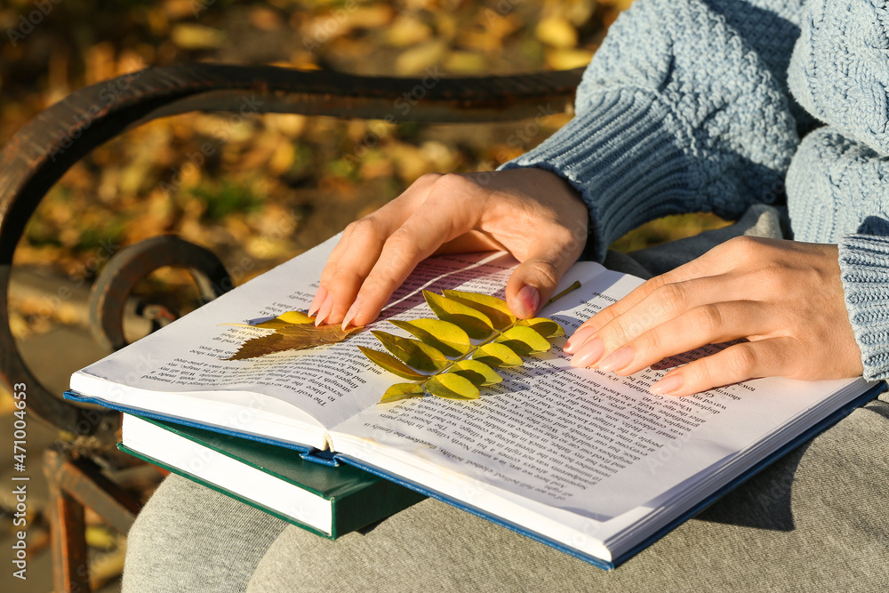 一个女人坐在长椅上，手里拿着打开的书和秋叶，特写