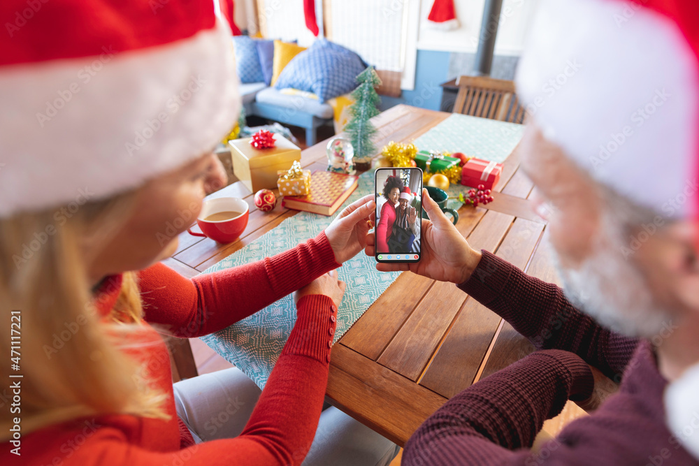 戴着圣诞老人帽的高加索夫妇与母女进行圣诞智能手机视频通话